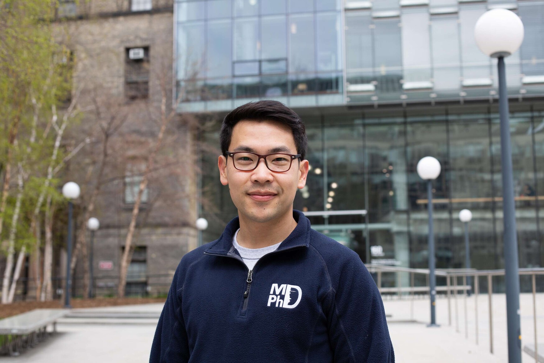 Alumnus Ben Ouyang wears a blue MD/PhD sweater and stands outside U of T's Donnelly Centre for Cellular and Biomolecular Research.